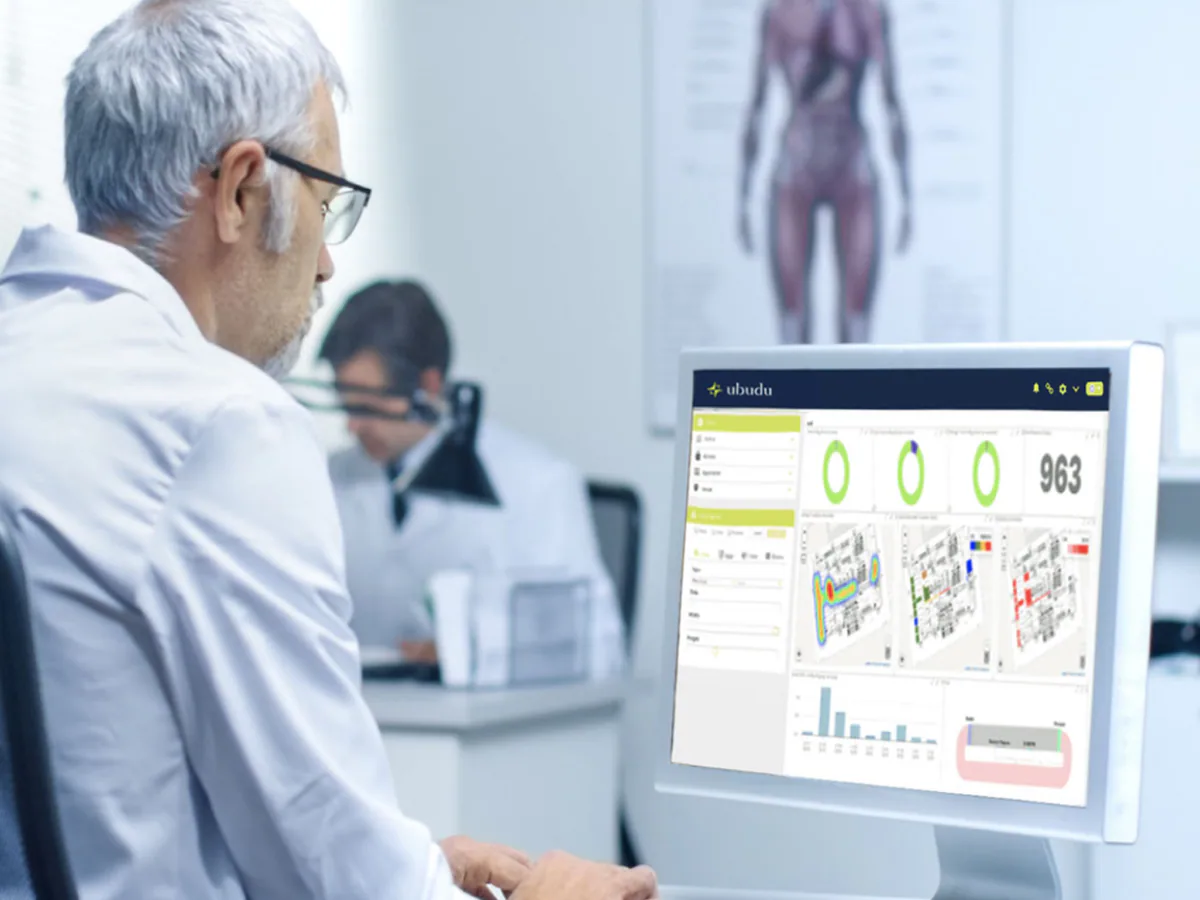Un soignant, à son bureau, consulte sur un écran le tableau de bord Ubudu RTLS : graphiques d'utilisation et cartes de chaleur des équipements de l'hôpital