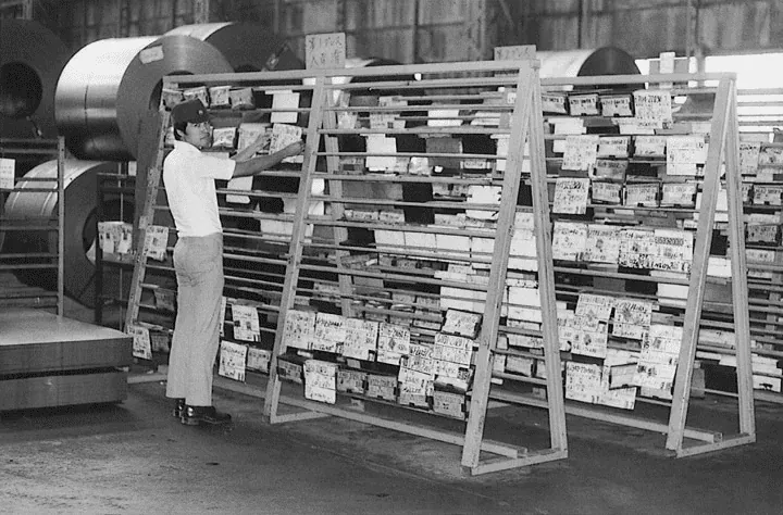 Fotografia de arquivo de um operário de fábrica junto a um quadro Kanban em papel, a forma manual de acompanhar as ordens de trabalho