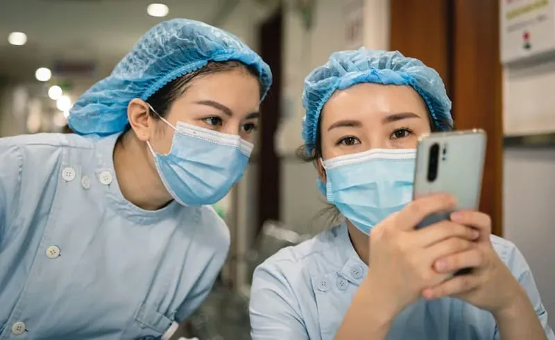 Duas enfermeiras de máscara a consultar um smartphone, ilustrando o wayfinding móvel em hospitais