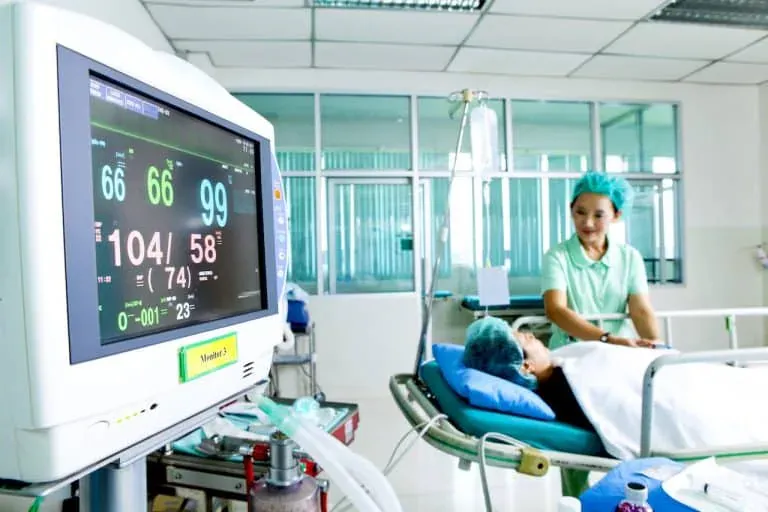 Enfermeira a cuidar de um paciente numa cama de hospital, com um monitor de paciente em primeiro plano