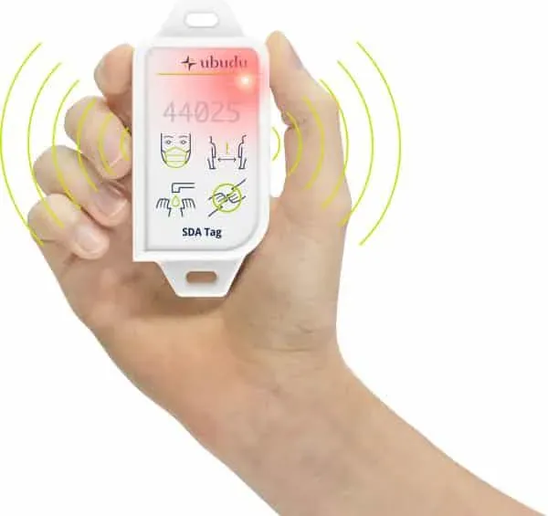 Mão a segurar a etiqueta Ubudu Social Distancing Assistant, a vibrar e iluminada para alertar para um contacto próximo