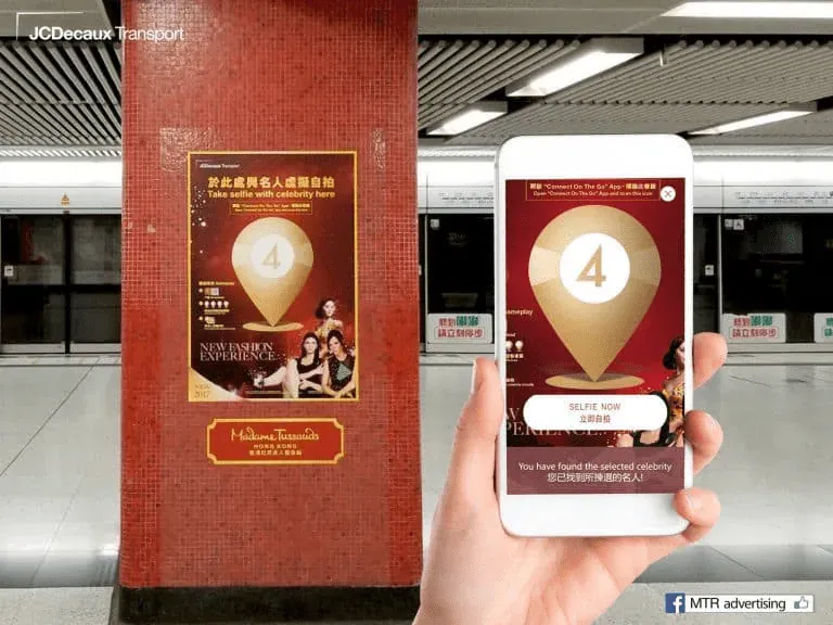 Smartphone showing a wayfinding checkpoint in front of a Madame Tussauds poster in an MTR station