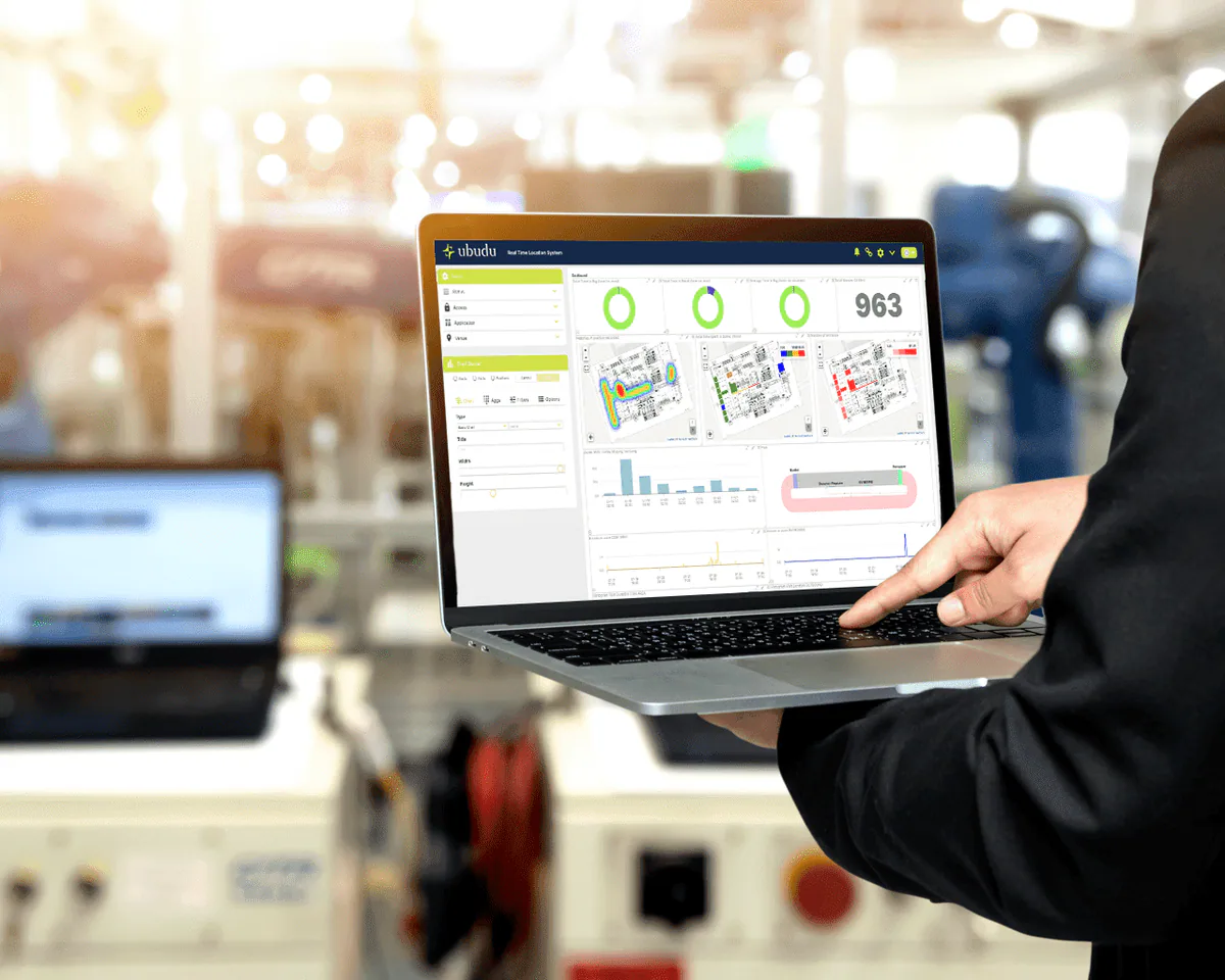 La dashboard Ubudu RTLS su un laptop in mano a un operatore in fabbrica, con indicatori di stato degli ordini di lavoro e una mappa planimetrica in tempo reale